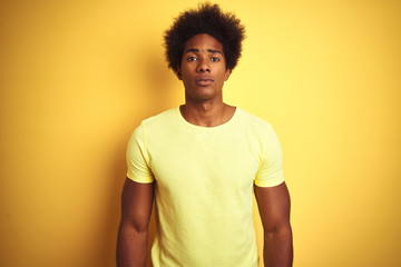 Fototapeta na wymiar African american man with afro hair wearing t-shirt standing over isolated yellow background with serious expression on face. Simple and natural looking at the camera.