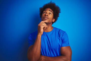 Obraz na płótnie Canvas African american man with afro hair wearing t-shirt standing over isolated blue background with hand on chin thinking about question, pensive expression. Smiling with thoughtful face. Doubt concept.