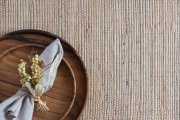 place setting on woven fiber background with two stacked wooden plates and linen napkin with yellow berries napkin ring