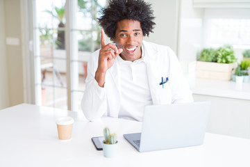 African American doctor man working with laptop at the clinic surprised with an idea or question pointing finger with happy face, number one