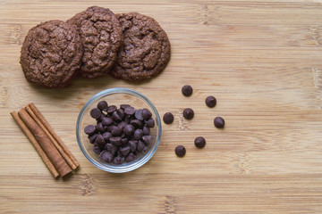 Chocolate chip brownie cookies with cinnamon displayed on a wooden cutting board; warm homemade chocolate cookies beside ingredients of cinnamon and chocolate chips