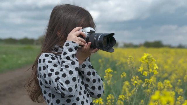 A child in nature with a camera. Cute little girl takes pictures in spring in nature. Young photographer.