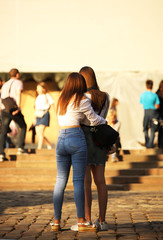 Naklejka premium Young long-haired brown-haired girls walk in the center of the ancient city. Fashion of modern youth. Free time and happy weekend. Blurred background. Ancient architecture and design of buildings