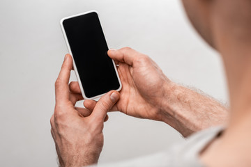 cropped view of man holding smartphone with blank screen isolated on grey