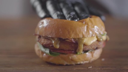 Hand of the chef in black rubber gloves pressing burger and sauce flows out close-up. Tasty food preparation. Juicy appetizing burger on the table. Slow motion.