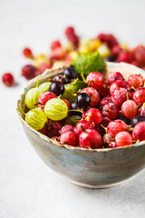 Red, green and black gooseberries in a bowl on gray background.