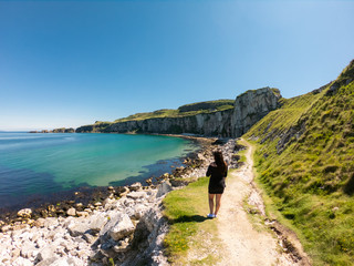 Young woman walking on path near Coast of Atlantic Ocean and Carrick Rede Rope Bridge 