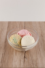 Three simple scoops of ice cream in a bowl: strawberry, vanilla and pistachio served on a wooden table