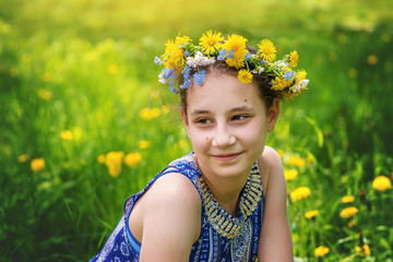 Teen  girl in a wreath of yellow dandelions on the background of spring grass.