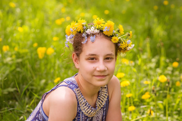 Teen  girl in a wreath of yellow dandelions on the background of spring grass.