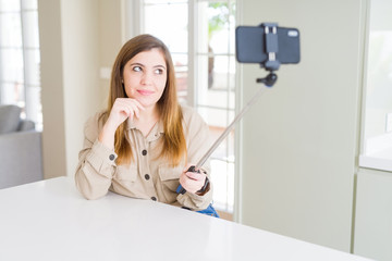 Beautiful young woman taking a picture using selfie stick serious face thinking about question, very confused idea