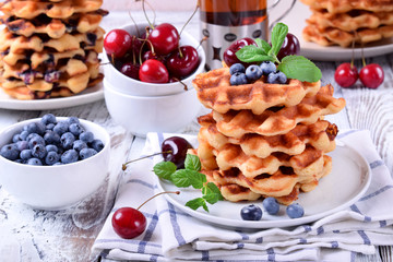 Stack of waffles topped with fresh bilberries, cherries and mint on the white wooden table