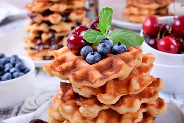 Stack of waffles topped with fresh bilberries, cherries and mint on the white wooden table