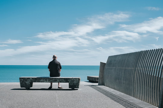 A man sitting on a wooden seat, looking out towards the sea