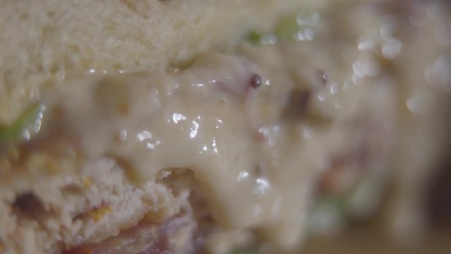 Macro view of tasty burger with sauce of cheese flowing out close-up. Tasty food preparation. Juicy appetizing burger details. Slow motion.