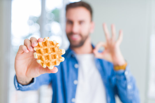 Handsome man eating sweet Belgian pancakes doing ok sign with fingers, excellent symbol