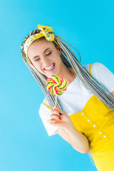 smiling girl with dreadlocks holding lollipop isolated on turquoise