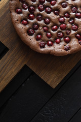 Yummy homemade chocolate cake with cherries on oak board on black background copy space