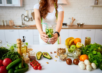 Obraz na płótnie Canvas Young woman drinking fresh water with cucumber, lemon and leaves of mint from glass in the kitchen. Healthy Lifestyle and Eating. Health, Beauty, Diet Concept.