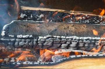 Wooden burning hot charred planks of wood logs in a fire with tongues of fire and smoke. Texture, background
