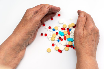 Old hands hold multicolored medical pills and tablets for ingestion from diseases on a white background.