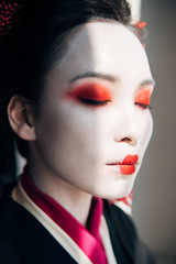 portrait of beautiful geisha with red and white makeup with closed eyes in sunlight