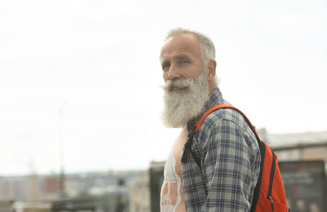 Active senior man walking in the city. Portrait of senior man with a beard while standing outside.