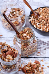 Granola with nuts in glass jars and cast iron pan on the white wooden table. Top view