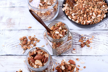 Granola with nuts in glass jars and cast iron pan on the white wooden table. Top view