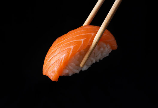 Traditional japanese nigiri sushi with salmon placed between chopsticks, separated on black background