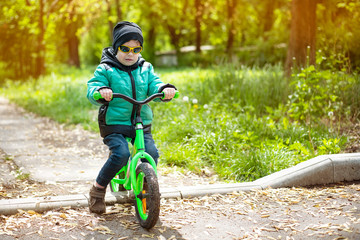 The young boy learns to ride a bicycle without pedals, the boy is a bit sad because he does not do well yet