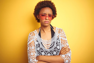 Young african american woman with afro hair wearing bikini and heart shaped sunglasses skeptic and nervous, disapproving expression on face with crossed arms. Negative person.