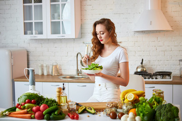 Young happy woman eating salad in the beautiful kitchen with green fresh ingredients indoors. Healthy food concept