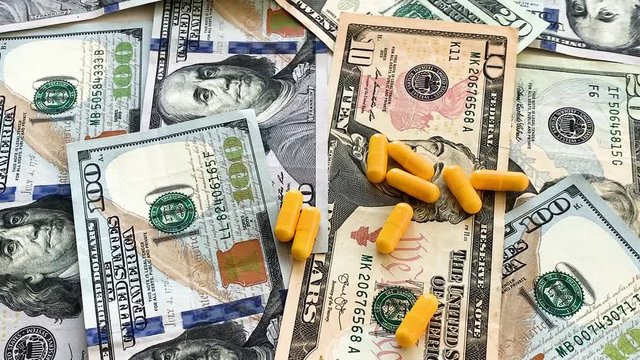 Expensive medicine. Pills of different colors on money background