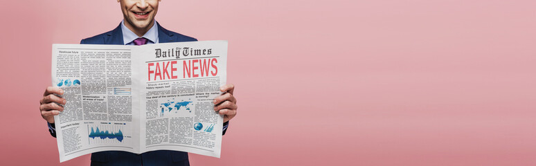 cropped view of smiling businessman reading newspaper with fake news on pink background, panoramic shot