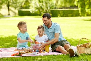 family, leisure and people concept - happy father and two little sons having picnic at summer park