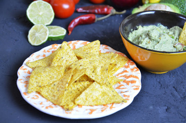 Mexican corn chips nachos with salsa dip on a black background with guacamole sauce, avacoda with lime and hot pepper
