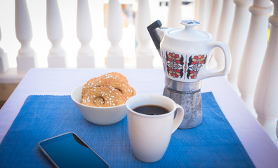 Breakfast or break outdoor on the balcony with coffe cup and homemade biscuits. Mobile phone in the corner. Vintage ceramic coffee maker