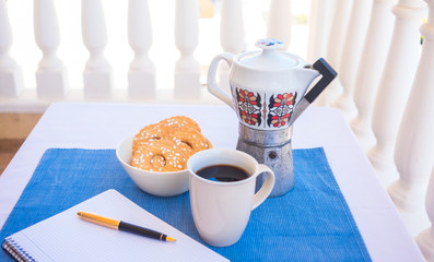 Breakfast or break outdoor on the balcony with coffe cup and homemade biscuits. Notebook and pen for writing. Vintage ceramic coffee maker