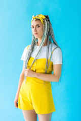 dissatisfied girl with dreadlocks looking at camera on turquoise