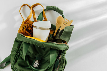 Green backpack with mesh market bag, bamboo cutlery  and  reusable coffee mug. Sustainable...