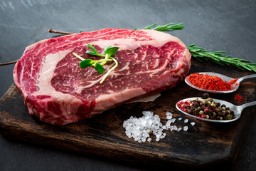 Fresh raw Rib eye Steak with seasonings and red pepper on cutting Board on grey background, close up