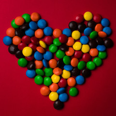 Frame of multicolor candy on a red background with the shape of a heart.