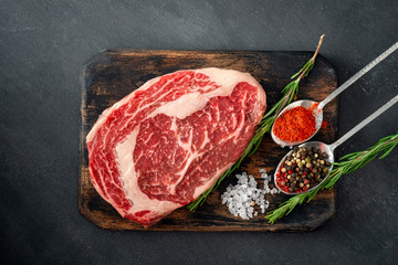 Fresh raw Rib eye Steak with seasonings and red pepper on cutting Board on grey background, close up and top view