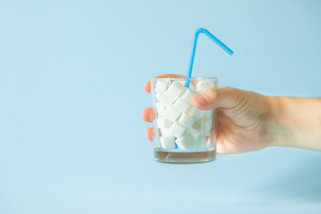 Excessive sugar consumption concept - hand holding glass with sugar cubes, copy space