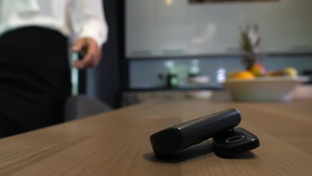 Close-up of key fob with car key lying on kitchen table while blurry on background hand of businesswoman driver in formal clothing taking it. Businesswoman going to drive