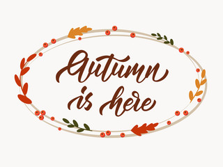 Autumn is here - hand lettering inscription on white background. Ellipse frame with autumn leaves and rowan berries. Vector illustration.