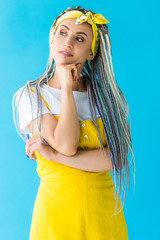 thoughtful girl with dreadlocks propping chin with hand isolated on turquoise