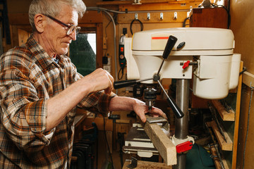 Amateur senior carpenter at his workshop, using bench drilling machine