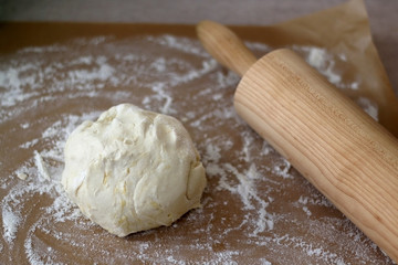 Ball of dough with flour and rolling pin on parchment paper. Selective focus.